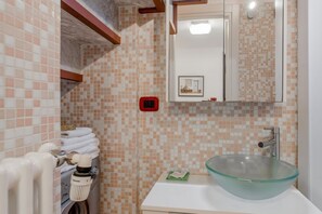 Een badkamer met een betegelde spatwand, een glazen wastafel en een handdoekrek met keurig opgevouwen handdoeken.