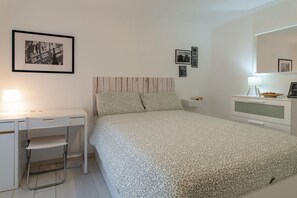 Een slaapkamer met een bed, bureau, stoel, kast en spiegel.