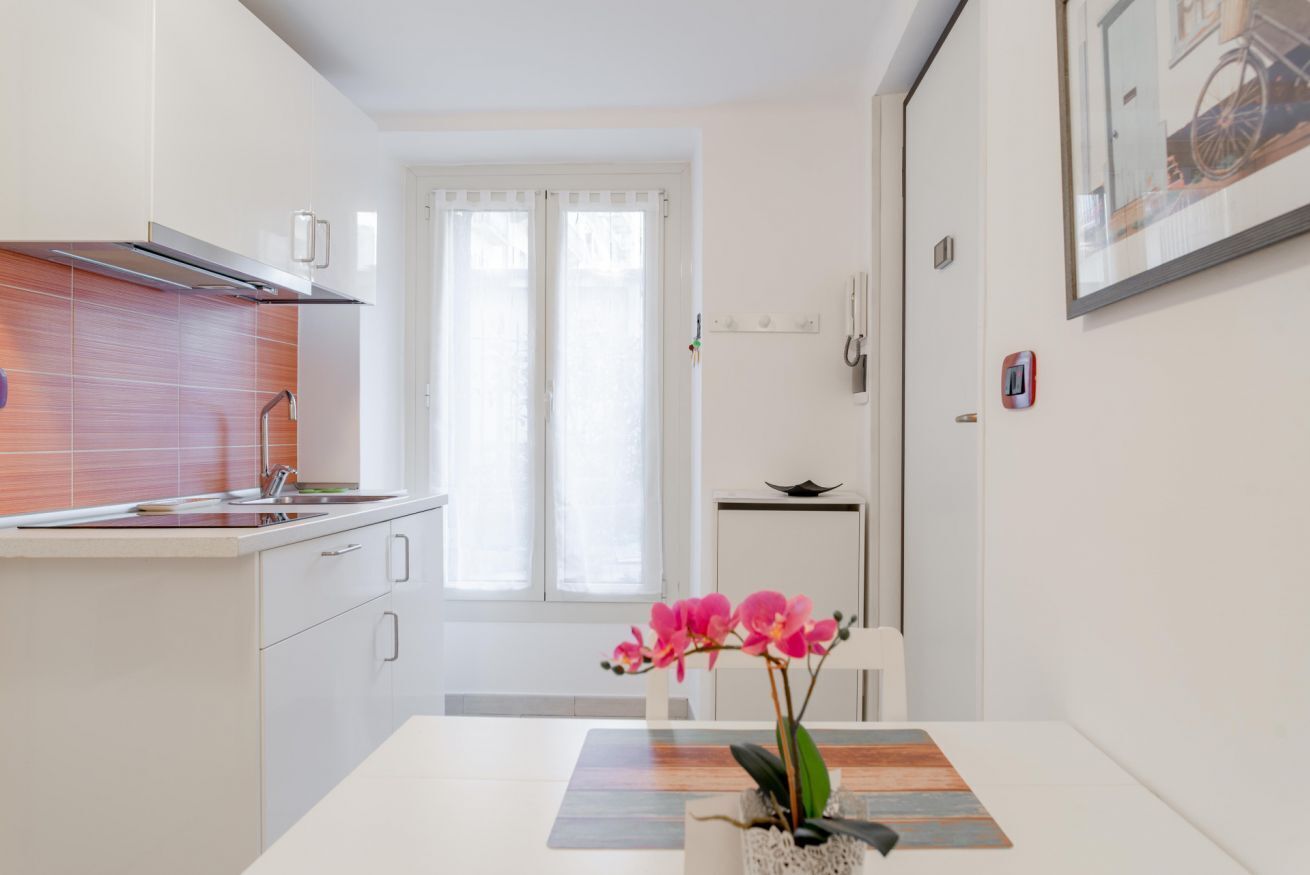 A modern kitchen with white cabinets, a stainless steel range hood, and a window with sheer curtains.