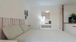 Een slaapkamer met een bed, nachtkastje, spiegel, televisie en radiator.