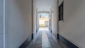 En smal hall med ett klinkergolv och vita väggar, som leder till ett öppet område med ett fönster och en dörr.