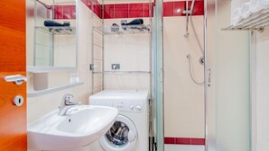 Een badkamer met een wasmachine, een wastafel, een douche en een spiegel.