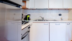 Een kleine keuken met witte kastjes, een kookplaat, een spoelbak en een koffiezetapparaat.