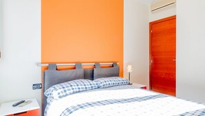 Een slaapkamer met een bed, een nachtkastje, een stopcontact en een houten deur.