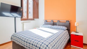 Een slaapkamer met een bed, een aan de muur bevestigde televisie, een raam en een rode kast.