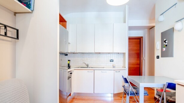 Een kleine keuken met witte kasten, een inbouwoven en een eethoekje met een glazen tafel en stoelen.