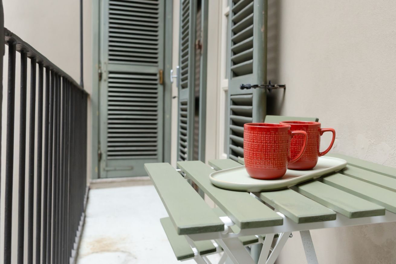 Una mesa verde al aire libre con dos tazas rojas sobre una bandeja blanca.
