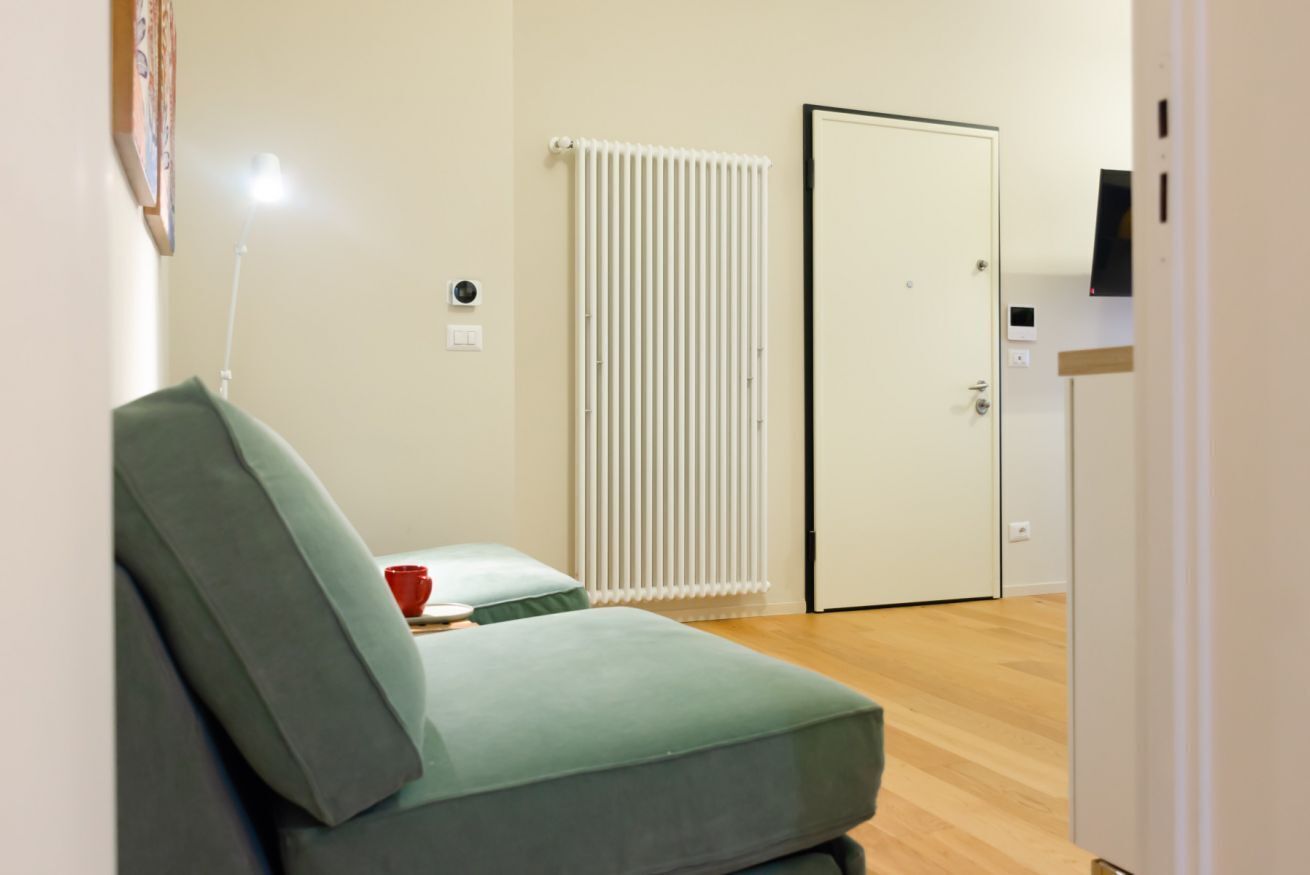 A room with a green sofa, a radiator, a door, and a small table with a red cup.