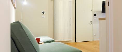 A room with a green sofa, a radiator, a door, and a small table with a red cup.