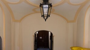 Ein Flur mit einer Holztür am Ende, einem schwarzen Laternenlicht, das von der Decke hängt, und einem Mülleimer auf der rechten Seite.