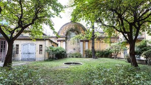 A courtyard with a fountain, surrounded by trees and a building with a large arched entrance.