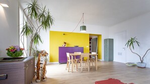 A bright living room with a wooden floor, a red bench, a purple cabinet, and a yellow wall.