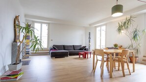 A modern living room with a sofa, dining table, chairs, and potted plants.
