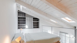 A bedroom with a loft bed, skylight, and built-in shelving.