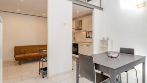 A modern kitchen with white cabinets, a dining table with chairs, and a sofa in the living area.