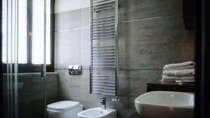 Un baño moderno con cabina de ducha de vidrio, dos inodoros, un bidé, un lavabo y un perchero para toallas.