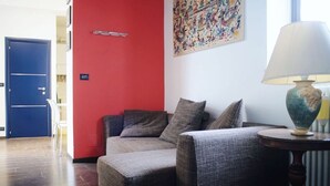 Una habitación con un sofá gris, una pared de acento roja, una puerta azul y una lámpara sobre una mesita de noche.