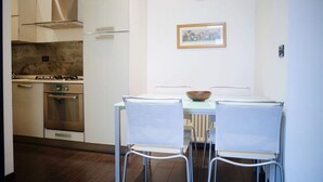 Una cocina con armarios blancos, estufa a gas, horno y una mesa de comedor con dos sillas.