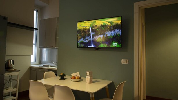 A modern kitchen with a dining area, a flat-screen TV mounted on the wall, and a small table with chairs.