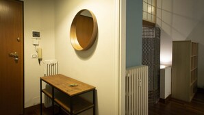 A hallway with a wooden door, a round mirror on the wall, a small table with a chair, and a radiator.