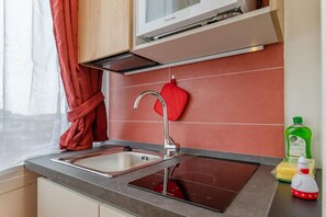 Een moderne keuken met een inbouwoven, een roestvrijstalen spoelbak en een rode ovenhandschoen aan de muur.