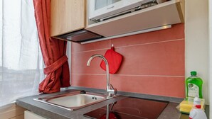 Una cocina con un lavamanos de acero inoxidable, un guante de horno rojo y una botella verde de detergente.