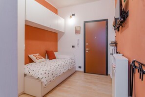 Een kleine, compacte slaapkamer met een enkel bed, een kledingkast, een deur en een kleine kitchenette.