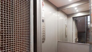 Interior de ascensor con puerta metálica, panel de control con botones y señal de seguridad.