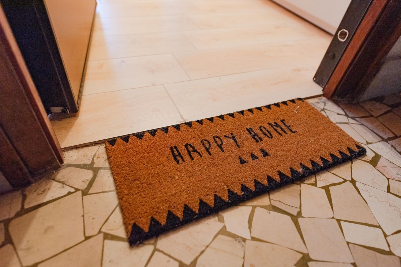 A brown doormat with "HAPPY BONE" written on it, placed at the entrance of a room with a tiled floor.
