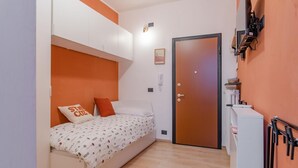 Una habitación pequeña y funcional con cama, puerta y un área de cocina compacta.