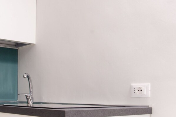 Una cocina moderna con una encimera oscura y elegante, un grifo de acero inoxidable y una pared blanca con toma de corriente.