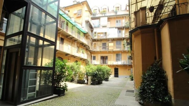 A courtyard with a cobblestone path, potted plants, and a glass entrance. - The Nest by Happyhstorino (Torino)