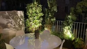 A round table with chairs on a wooden deck, surrounded by potted plants and a metal fence. - The Nest by Happyhstorino (Torino)