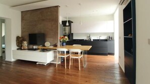 A modern living room with a wooden floor, a white entertainment unit, and a dining area with a table and chairs. - The Nest by Happyhstorino (Torino)