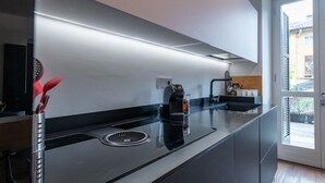 A modern kitchen with a black countertop, a coffee machine, and a window with blinds. - The Nest by Happyhstorino (Torino)