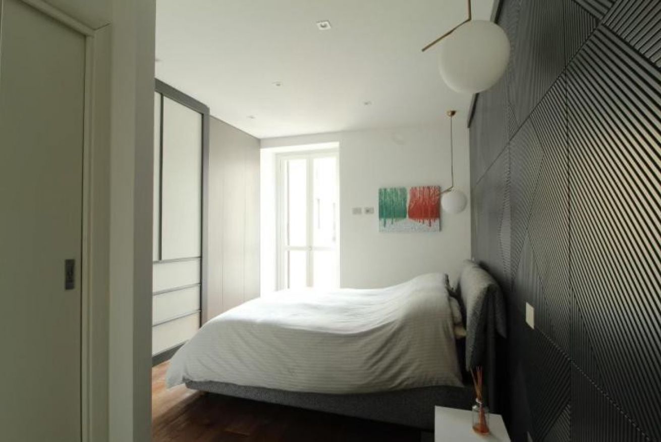 Une chambre à coucher comprenant un lit, une table de chevet, une fenêtre et un mur orné d’un motif géométrique.
