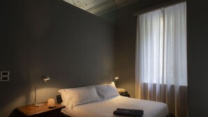 Une chambre d’hôtel avec un lit, deux lampes de chevet, une table de chevet et une fenêtre avec des rideaux légers.