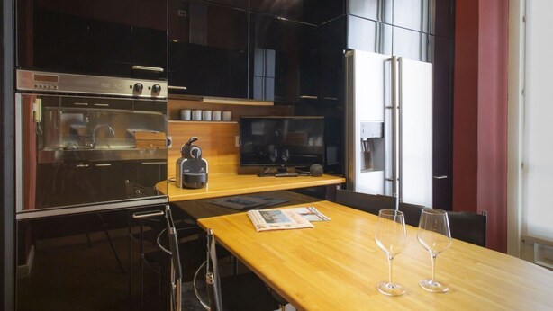 Une cuisine moderne équipée d’appareils électroménagers en acier inoxydable, une table à manger en bois et un téléviseur.