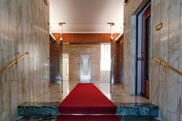 A marble-floored hallway with a red carpet leading to a door, flanked by glass doors and wooden panels.