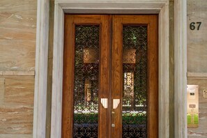 A wooden double door with decorative metal grilles, a stone wall, and a building number 67.