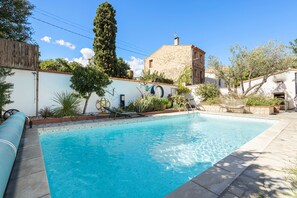 Una piscina con un muro in pietra, un albero alto e un edificio con l'orologio.