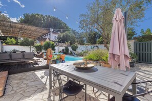 Un'area patio con tavolo, sedie, una piscina e una zona relax coperta.
