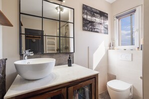 Un bagno con un lavandino bianco capiente, uno specchio, un water e una finestra con vista.