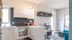 Une cuisine moderne avec des meubles blancs, un four encastré et un coin bar avec des tabourets.
