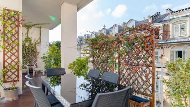 Une terrasse extérieure aménagée avec des meubles en osier, une table et une vue sur les bâtiments adjacents.