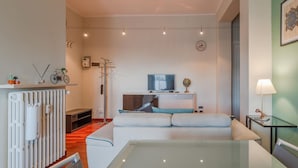 A modern living room with a glass dining table, a sofa, a television, and a radiator. - [AC] La Finestra Sulla Mole (Torino)