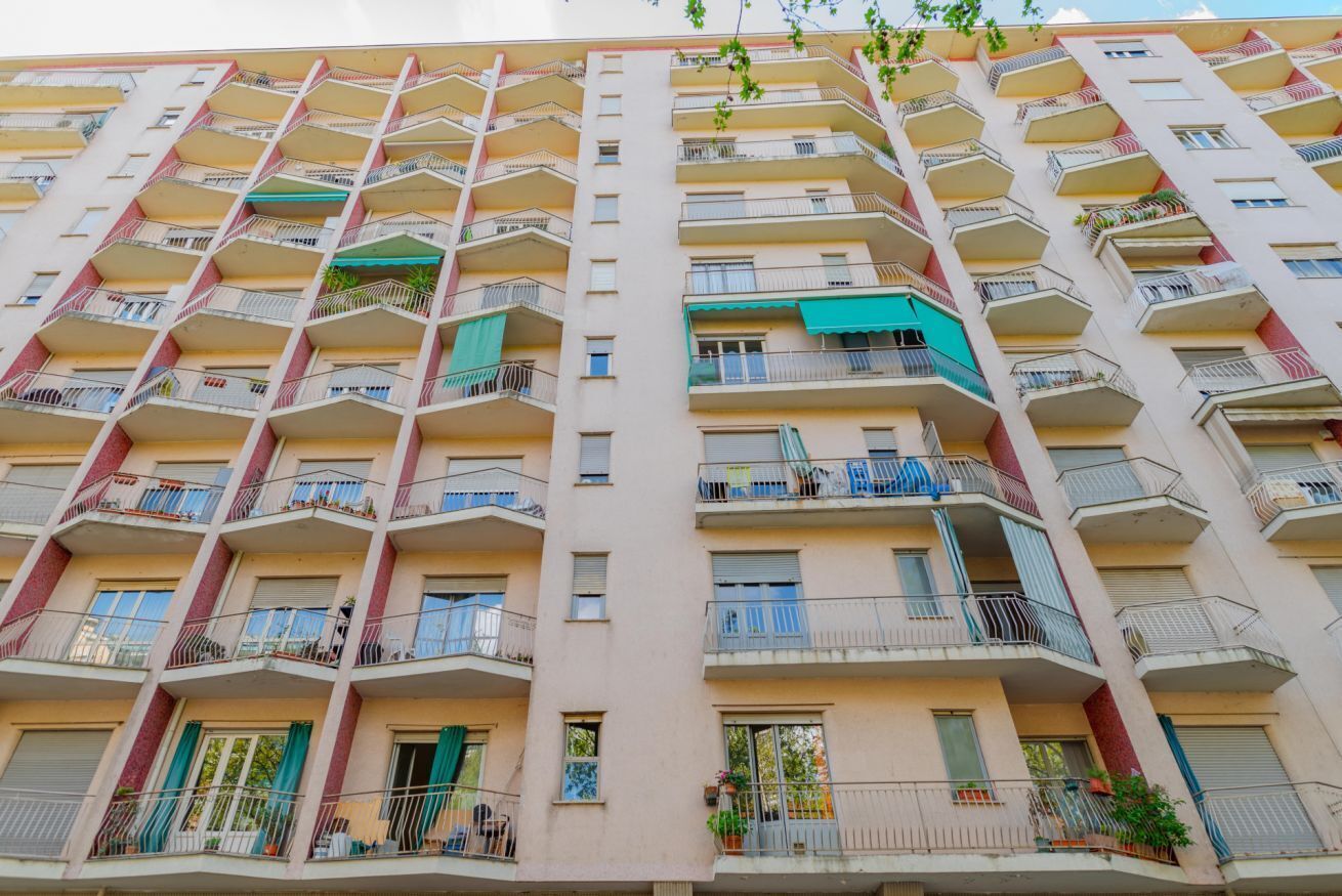 A multi-story residential building with balconies, windows, and some greenery.