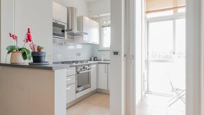 A modern kitchen with white cabinets, a stainless steel range hood, and a built-in oven. There are potted plants on the counter, and a sliding glass door leading to an outdoor area. - [AC] La Finestra Sulla Mole (Torino)