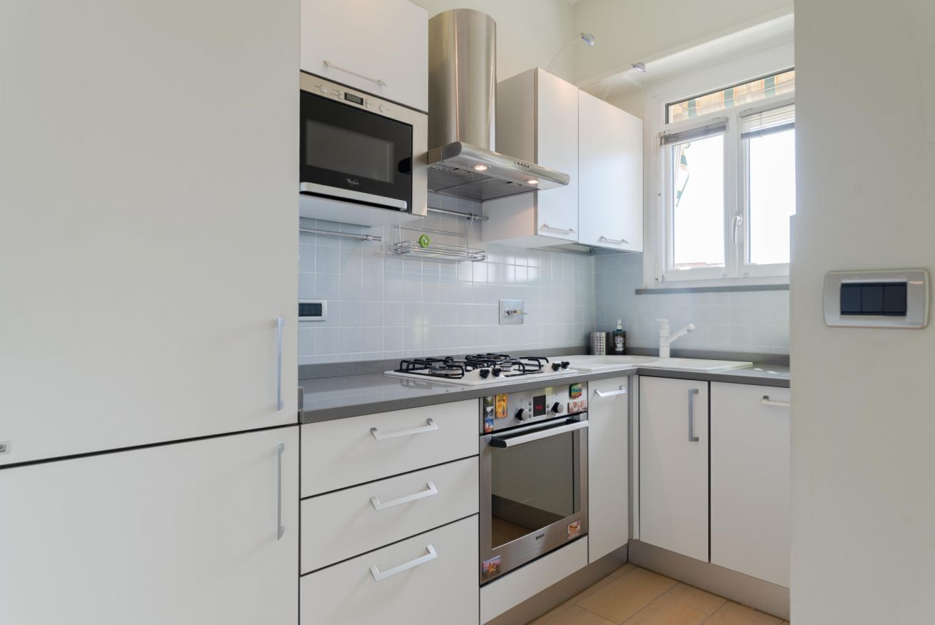 A modern kitchen with white cabinets, a built-in oven, a gas stove, and a stainless steel range hood.