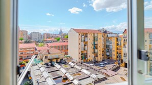 A view of a cityscape with a prominent yellow building with balconies, a tower in the background, and a clear sky. - [AC] La Finestra Sulla Mole (Torino)